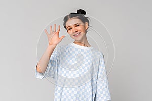 Portrait of cute dark-haired teen girl saying hi, waving hand and smiling friendly, introducing herself, greeting, standing in