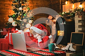 Portrait of cute dreamy Santa helper writing letter to Santa Claus Child type letter to Santa Santa helper using