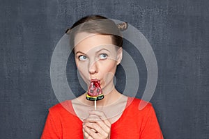 Portrait of cute dreamy young woman eating sweet lollipop