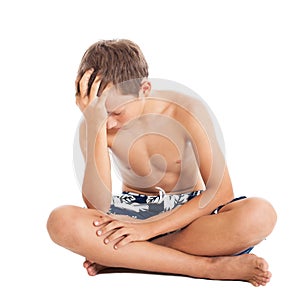 Portrait of a cute european teen boy wearing swimming shorts. A boy sitting on the floor.