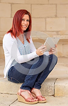 Portrait of a cute expressive redhead woman reading information on its touch pad