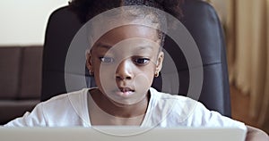 Portrait of cute focused 6 years old mixed race african american girl child pensively looking at laptop screen reading