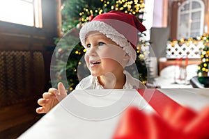 Portrait cute funny excited toddler baby boy wear santa red hat hold big white gift box christmas present against