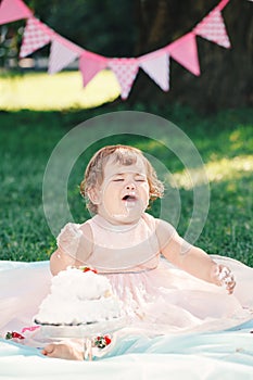 Portrait of cute funny upset sad crying Caucasian baby girl in pink tutu dress celebrating her first birthday