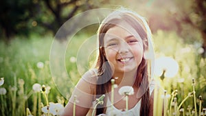 Portrait of cute girl blow on a dandelion in garden at sunset