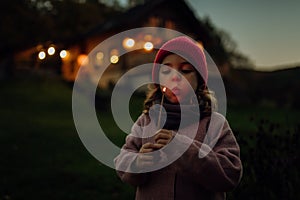 Portrait of cute girl blowing out flame on a burning stick. Family having a barbecue in the garden on an autumn evening.