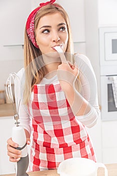 Portrait of a cute girl fingerlicking whisked egg whites with a hand whisk in the other hand