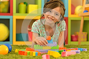 Portrait of cute girl playing with colorful plastic blocks in room