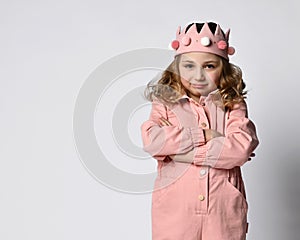 Portrait of a cute girl with a plush crown, stands with her arms crossed over her chest, in a closed pose. in a dusty