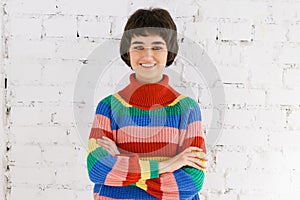 Portrait cute girl in rainbow sweater against white brick