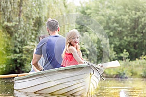 Portrait of cute girl sitting with father on rowboat in lake during summer