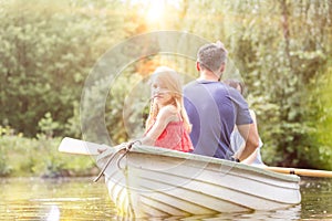 Portrait of cute girl sitting with father on rowboat in lake during summer