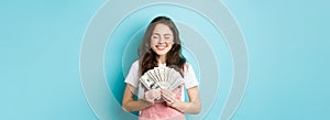 Portrait of cute girl smiling with satisfaction, holding money and looking pleased, winning prize in dollar bills