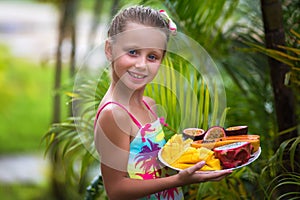 Portrait of a cute girl in the tropics. Girl holding a plate with exotic fruits