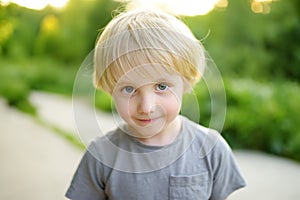 Portrait of a cute green-eyed blonde preschooler boy. Child walking in public park on summer day