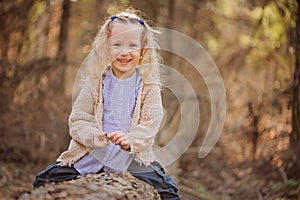 Portrait of cute happy child girl sitting on the tree in early spring forest