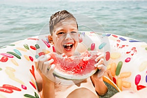 Cute happy little boy having fun in rubber ring eating juicy watermelon