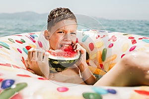 Cute happy little boy having fun in rubber ring eating juicy watermelon