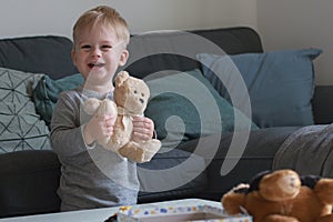 portrait of cute happy little boy playing with teddy bear in living room