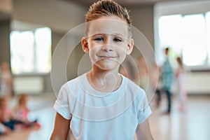 Portrait of a cute and happy little boy in white t-shirt looking at camera with smile while standing in the dance studio