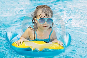 Portrait of cute happy little girl having fun in swimming pool, floating in blue refreshing water wit rubber ring, active summer v