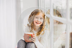 Portrait of cute happy little girl sitting on windowsill