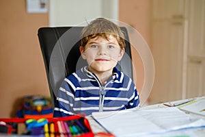 Portrait of cute happy school kid boy at home making homework. Little child writing with colorful pencils, indoors