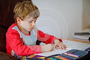 Portrait of cute happy school kid boy at home making homework. Little child writing with colorful pencils, indoors