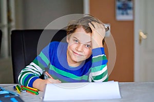 Portrait of cute happy school kid boy at home making homework. Little child writing with colorful pencils, indoors