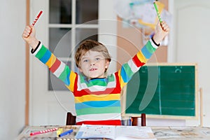 Portrait of cute happy school kid boy at home making homework. Little child writing with colorful pencils, indoors