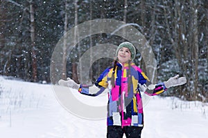 Portrait of cute happy teenage girl is catching snowflakes with her hands in winter