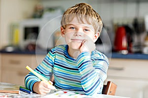 Portrait of cute healthy happy school kid boy at home making homework. Little child writing with colorful pencils