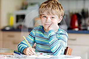 Portrait of cute healthy happy school kid boy at home making homework. Little child writing with colorful pencils