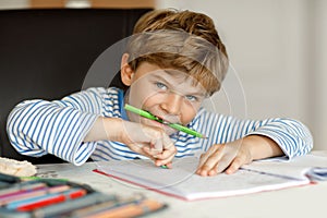 Portrait of cute healthy happy school kid boy at home making homework. Little child writing with colorful pencils