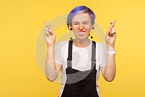 Portrait of cute hipster woman crossing fingers for good luck, wishing fortune and victory. yellow background, studio shot