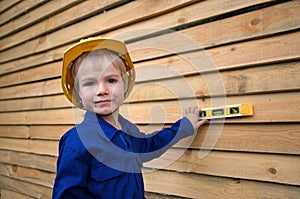 Portrait of cute inquisitive boy 6 years old in blue overalls and in construction helmet with level tool in hands