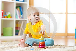 Portrait of cute kid boy assembling colorful pyramid toy on floor at living room