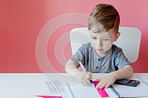 Portrait of cute kid boy at home making homework. Little concentrated child writing with colorful pencil, indoors. Elementary