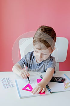 Portrait of cute kid boy at home making homework. Little concentrated child writing with colorful pencil, indoors. Elementary