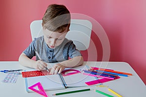 Portrait of cute kid boy at home making homework. Little concentrated child writing with colorful pencil, indoors. Elementary