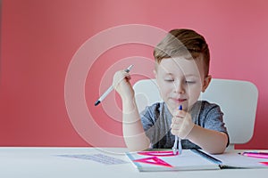 Portrait of cute kid boy at home making homework. Little concentrated child writing with colorful pencil, indoors. Elementary