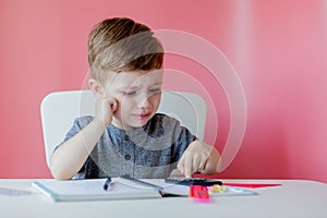 Portrait of cute kid boy at home making homework. Little concentrated child writing with colorful pencil, indoors. Elementary