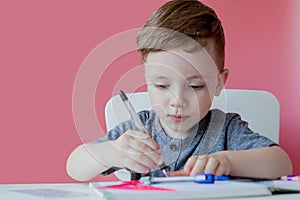 Portrait of cute kid boy at home making homework. Little concentrated child writing with colorful pencil, indoors. Elementary