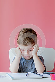 Portrait of cute kid boy at home making homework. Little concentrated child writing with colorful pencil, indoors. Elementary