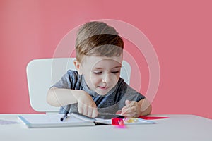 Portrait of cute kid boy at home making homework. Little concentrated child writing with colorful pencil, indoors. Elementary