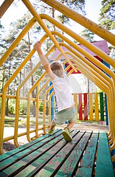 Portrait of cute kid boy playing on the climbing frame. Young boy climbing on playground during summer. Child climbing