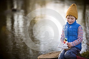 Portrait of cute kid boy playing with handmade ship. kindergarten boy sailing a toy boat by the waters` edge in the park