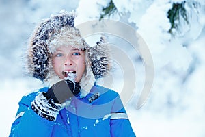 Portrait of cute kid boy trying to eat snow outdoors. Child having fun in a winter park