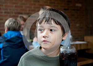 Portrait of Cute kid sitting on table with cold drink in restaurant, Child boy drinking soda or soft drink with straw, Child boy