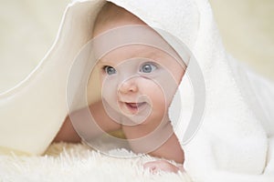 Portrait of a cute, laughing baby with a towel on a white bed. Innocence baby crawling on white bed with towel on his head at home